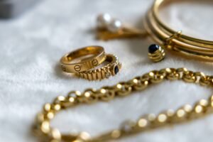 Collection of gold rings, bracelets, and chains with gemstones on a textured surface.